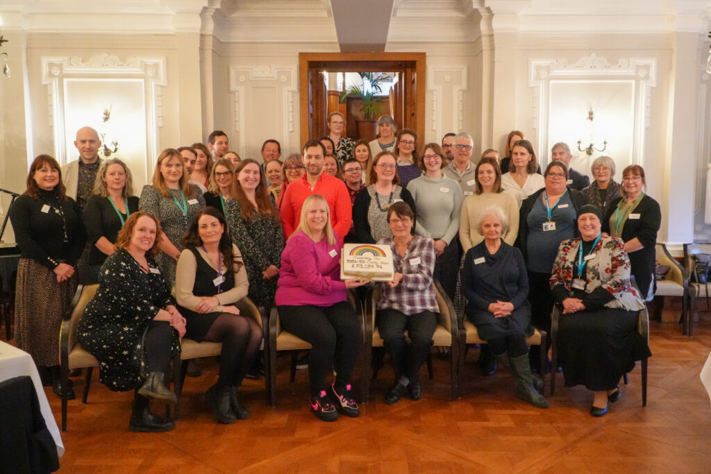 A large group of people stand smiling to celebrate an achievement.
