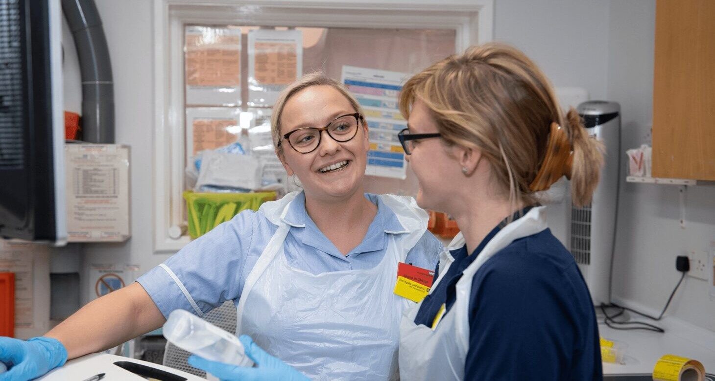 Nurse smiles at colleague in clinical environment