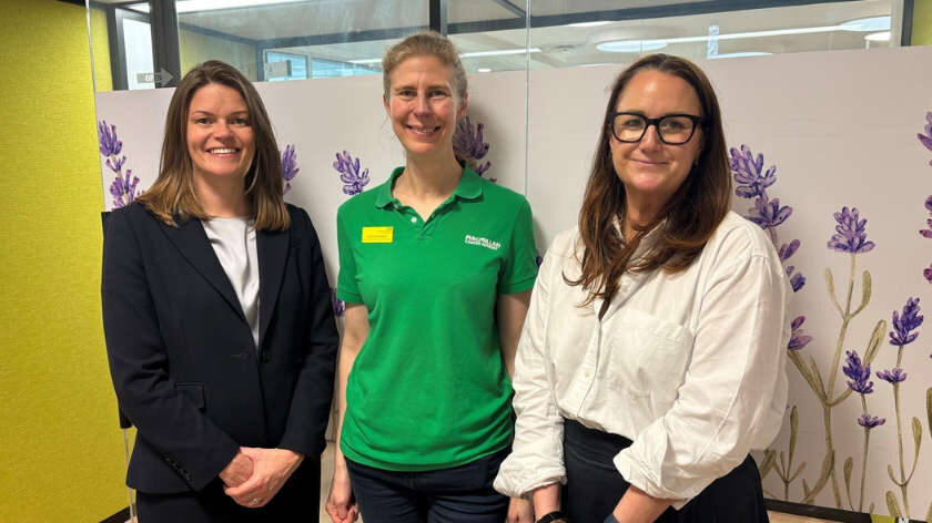 Three women stand smiling.