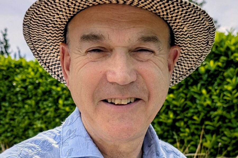 and image of john dean smiling he is wearing a hat and a blue shirt